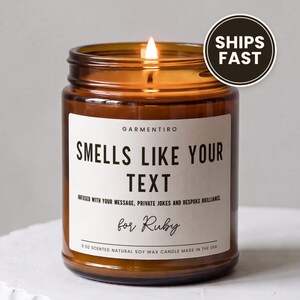 May include: A 9 oz scented natural soy wax candle in an amber glass jar with a lit wick. The white label reads: GARMENTIRO, SMELLS LIKE YOUR TEXT, INFUSED WITH YOUR MESSAGE, PRIVATE JOKES AND BESPOKE BRILLIANCE, for Ruby, 9 OZ SCENTED NATURAL SOY WAX CANDLE.