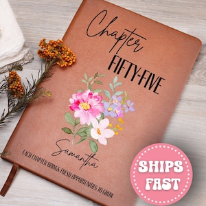 May include: A brown leather journal with the words "Chapter FIFTY-FIVE" and "Samantha" printed on the cover. The journal features a floral design with pink, purple, and white flowers. The text "Each chapter brings fresh opportunities to grow" is also printed on the cover.