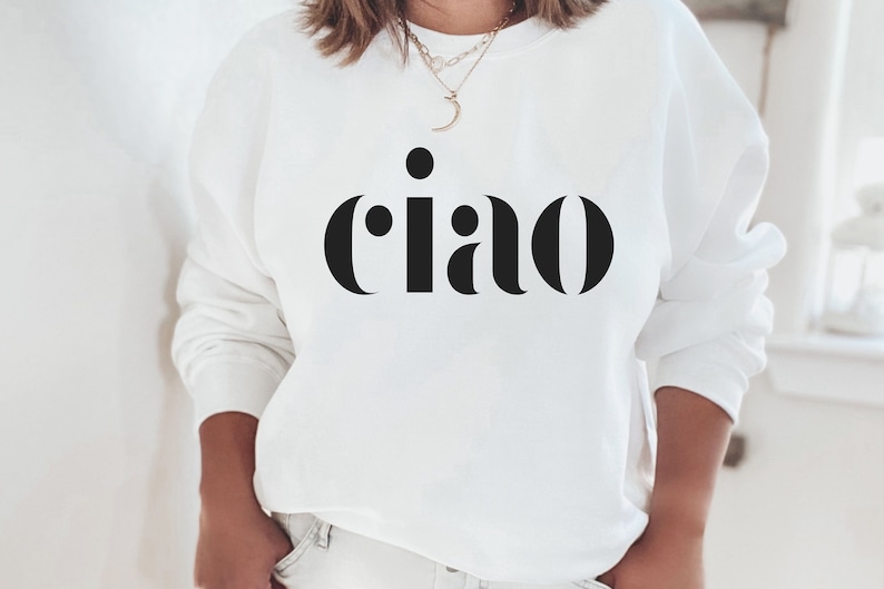 May include: White sweatshirt featuring the Italian greeting "ciao" in large, black lettering. The long-sleeved top has a crew neck. A simple, casual garment, perfect for everyday wear. The word "ciao" is a greeting.