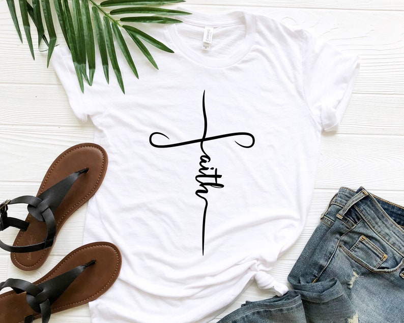 K&ouml;nnte beinhalten: Wei&szlig;es T-Shirt mit einem schwarzen Kreuz und dem Wort "faith" vertikal in der Mitte des Kreuzes.