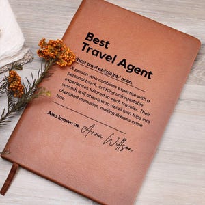 May include: A brown leather journal with the text "Best Travel Agent" and a definition of the term. The journal also includes the text "Also known as: Anna Willson".