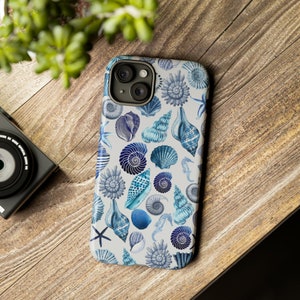 May include: A white phone case with a blue and white seashell pattern. The case has a camera lens cutout and a white background.