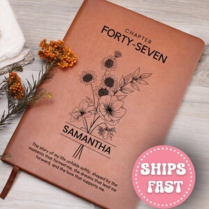 May include: A brown leather journal with the text "CHAPTER FORTY-SEVEN" and "SAMANTHA" printed on the cover. A floral illustration is above the name. The journal also has an inspirational quote. A pink sticker with the words "SHIPS FAST" is visible.