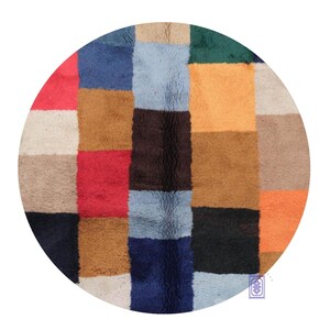 Peut inclure: Un tapis rond multicolore avec un motif patchwork. Le tapis présente des carrés de différentes couleurs, dont le rouge, le bleu, le marron et l'orange. Le tapis a un aspect texturé, suggérant une construction tissée ou touffetée. Un élément de décoration intérieure.