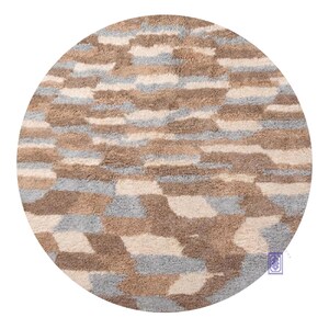 Peut inclure: Un tapis rond avec un motif géométrique. Le tapis présente un mélange de couleurs, notamment beige, marron et bleu clair, disposées en un motif répétitif. Le tapis a un aspect doux et texturé, suggérant un toucher confortable.
