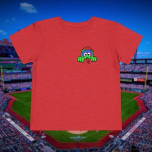 May include: Red t-shirt with a green, blue, and red cartoon character wearing a red hat peeking out from behind the shirt.