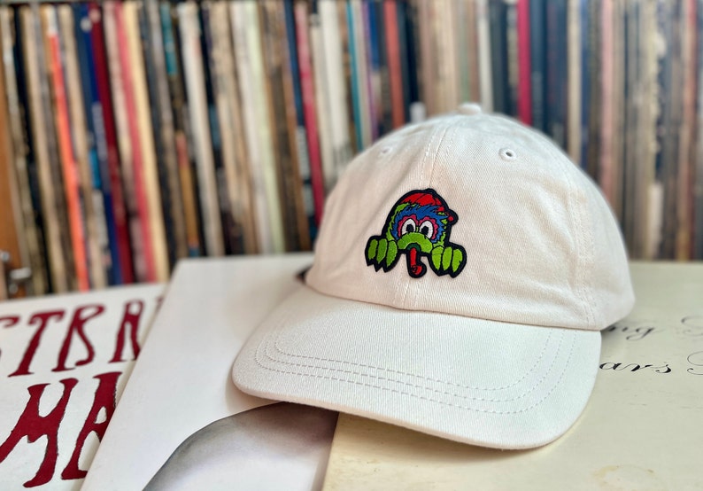 May include: White baseball cap with a green, blue and red cartoon monster patch on the front.