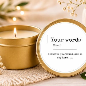 May include: A gold-coloured metal candle tin with a lit white wax candle inside. The lid is placed upright next to the tin, featuring a white label with the black printed text: Your words (Noun) Whatever you would like to say here .....