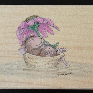 May include: A wooden stamp featuring a whimsical illustration of a mouse resting in a nest under a large pink flower. The mouse is brown with closed eyes, and the flower has green and purple hues. The stamp is dated 2008.