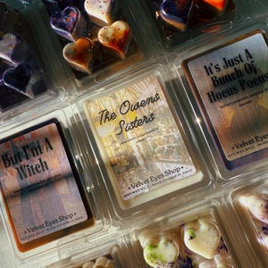 May include: Heart-shaped soy wax melts in clear plastic containers. The melts are various colors, including purple, orange, and white. The image also shows labels with text: "But I'm A Witch", "The Owens Sisters", and "It's Just A Bunch Of Hocus Pocus".
