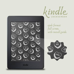 May include: A black and white Kindle e-reader with a heart-shaped pattern on the screen. The pattern includes phrases like "Slow Burn", "Fated Mates", and "Enemies to Lovers". The text "kindle" is displayed on the bottom of the e-reader.