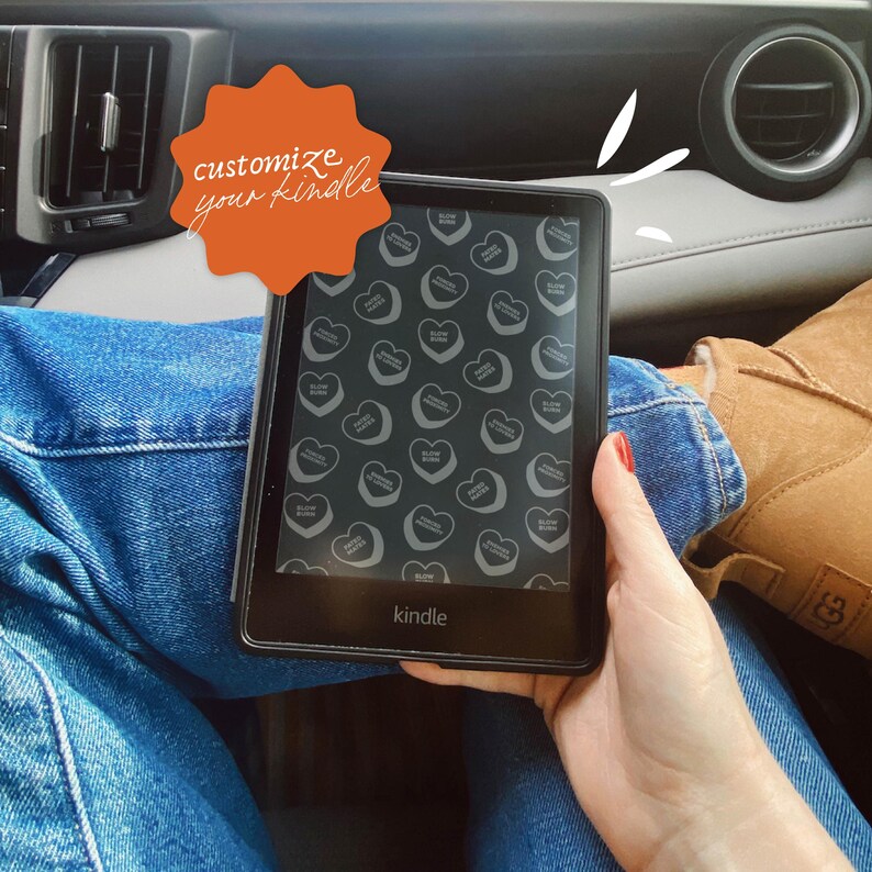 May include: A black Kindle e-reader with a custom screen saver featuring a pattern of small white hearts on a black background. The text "customize your kindle" is written on a bright orange starburst sticker.