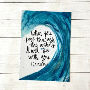 May include: Watercolor painting of a blue wave with the text "when you pass through the waters I will be with you ISAIAH 43:2" in black calligraphy.
