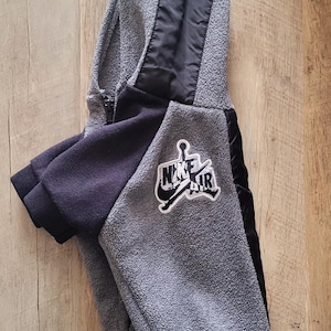 K&ouml;nnte beinhalten: Eine wei&szlig;e Keramik-Tasse mit schwarzem Henkel und dem Text "But First, Coffee" in fetter, schwarzer Schrift. Die Tasse steht vor einem verschwommenen Hintergrund, der eine gem&uuml;tliche Umgebung suggeriert.