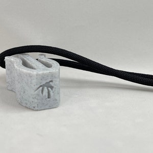 May include: A speckled gray whistle with a black cord attached. The whistle has a palm tree design etched on the side. The black cord is knotted at the end.