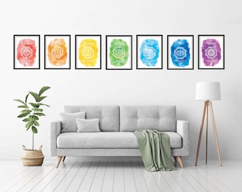 May include: Seven framed prints of the seven chakras, each with a watercolour background in a different colour of the rainbow. The prints are arranged in a row on a white wall above a grey sofa.