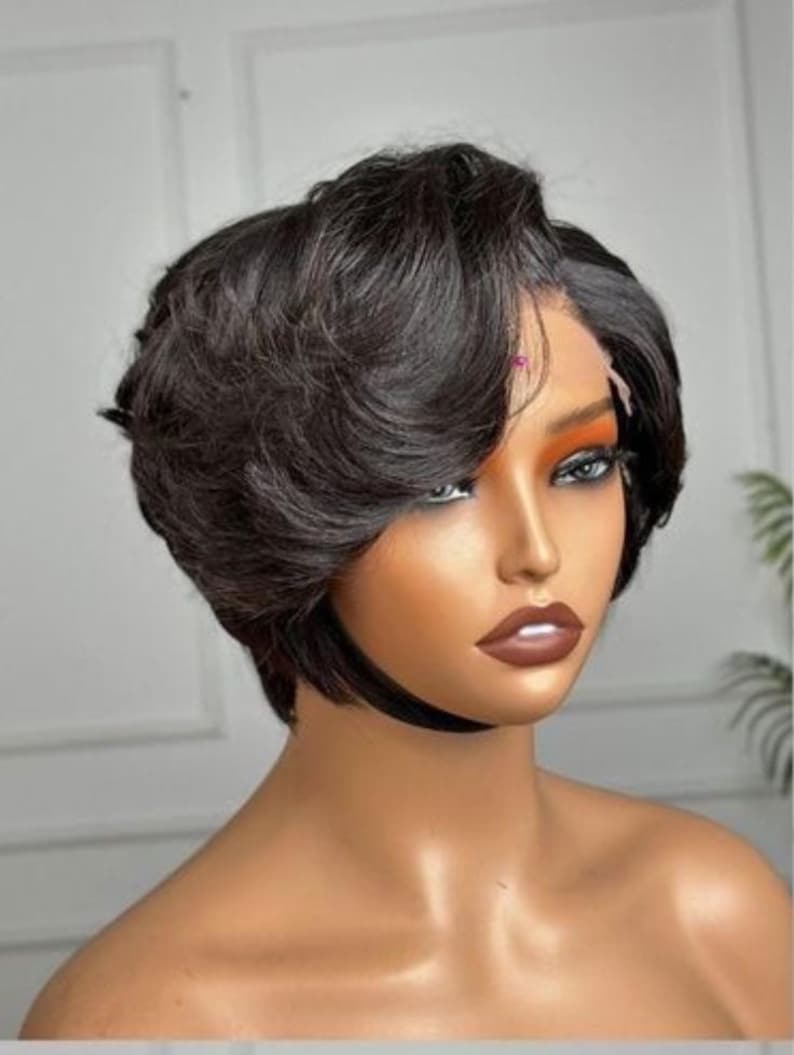 May include: A short, dark brown wig with a side parting and layered style. The wig has a natural-looking hairline and is styled with soft waves. The wig is designed to be worn by anyone.