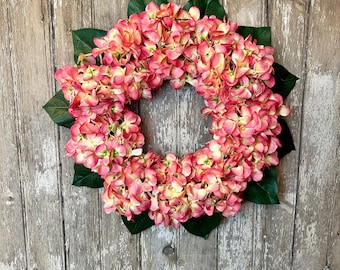 May include: A pink and white hydrangea wreath with green leaves. The wreath is made of silk flowers and is perfect for decorating a door or wall.