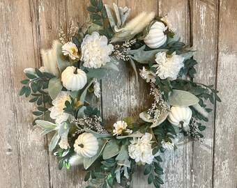 May include: A white and green fall wreath with white pumpkins, white flowers, and green leaves.