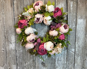 May include: A pink and white peony wreath with greenery. The wreath is made of silk flowers and is perfect for a spring or summer wedding.