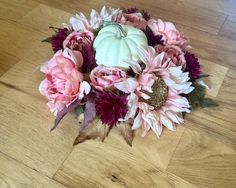 May include: A white pumpkin centerpiece surrounded by pink and burgundy flowers. The flowers are arranged in a circle around the pumpkin, creating a beautiful and festive display.