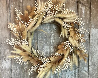 May include: A fall-themed wreath with dried grasses, brown leaves, and white berries.