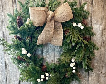 May include: A green Christmas wreath with a burlap bow and white berries. The wreath is decorated with pine cones and other natural elements.