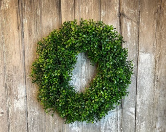 May include: A green artificial boxwood wreath hanging on a weathered wooden door.