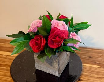 May include: A wooden box filled with a bouquet of pink and red roses. The roses are arranged in a rustic wooden box.