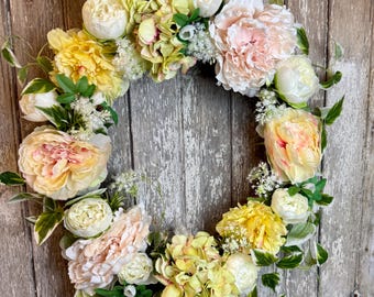 May include: A floral wreath featuring a variety of flowers in shades of yellow, white, and peach. The wreath is adorned with green leaves and is set against a weathered wooden background, creating a rustic aesthetic.