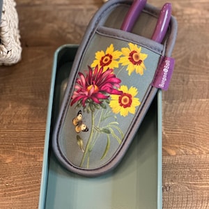 May include: A gray gardening tool holder with a floral print featuring yellow sunflowers, pink flowers, and a butterfly. The holder has two purple gardening shears inside and the text "Burgoyne & Ball" on the side.