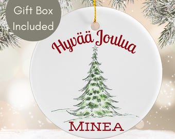May include: White ceramic Christmas ornament with a green Christmas tree illustration and the text "Hyvää Joulua Minea". Includes a gold string for hanging. Made in the USA.
