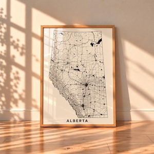 May include: A framed wall art print featuring a black and white map of Alberta, Canada. The map displays detailed road networks, geographical terrain, and water bodies. The word ALBERTA is printed in bold black capital letters at the bottom.