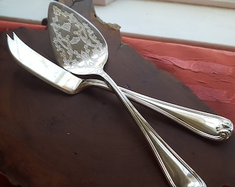 May include: A silver cheese knife and a silver cake server with an ornate design on a wooden surface.