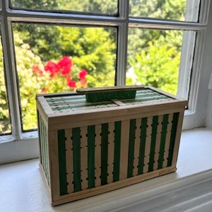 May include: A small wooden box with a green and white striped design. The box has a hinged lid and a small handle on top.