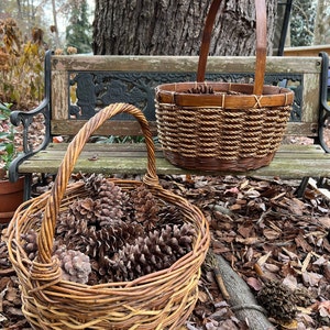 May include: Two wicker baskets, one filled with pine cones, sitting on a wooden bench in front of a tree.