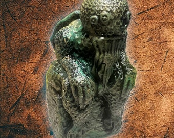 May include: A green and brown sculpted figurine of a creature with a large head and multiple eyes. The creature has a long, flowing beard and appears to be sitting with its arms crossed.