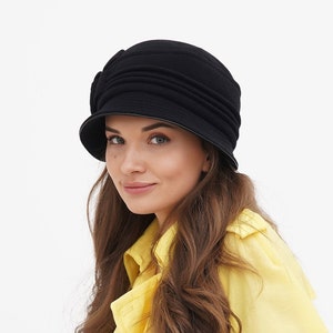 Woman wearing a black cloche hat, posed against a white backdrop.