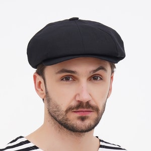 Puede incluir: Una gorra de newsboy negra con una visera ligeramente curvada. La gorra está hecha de un tejido suave y texturizado.