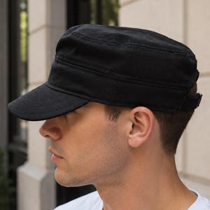 Peut inclure: Une casquette militaire noire unie de style cadet avec un dessus plat, une visière courte et incurvée, et une sangle réglable à l'arrière. La casquette est fabriquée dans un tissu résistant avec des coutures visibles sur la calotte et le bord.