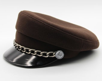 May include: A brown felt cap with a black leather brim and a silver chain detail. The cap has a silver button with a design on it.
