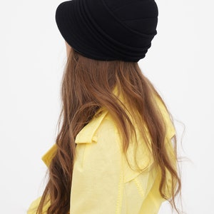 Rear view of a woman wearing a black cloche hat, highlighting the hat's back design, set against a white backdrop.