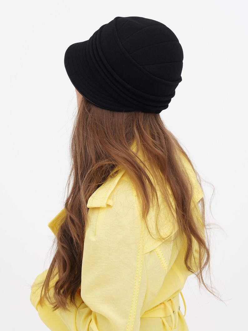 Rear view of a woman wearing a black cloche hat, highlighting the hat's back design, set against a white backdrop.