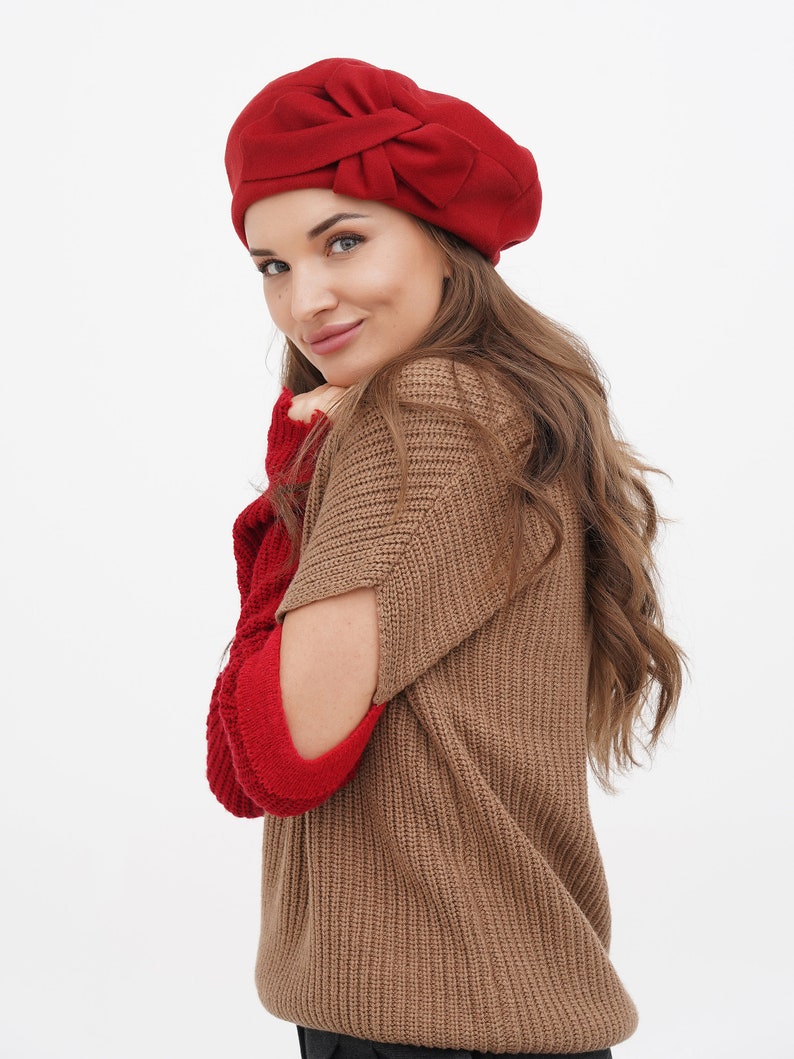 Chic woman in a red beret featuring a bow detail, against a white backdrop.