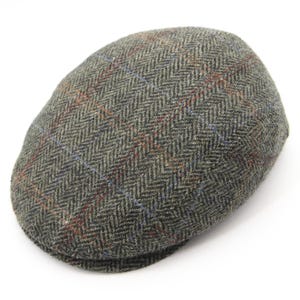 Op de afbeelding: Grijze tweed flat cap met visgraatpatroon. De pet heeft een ruitpatroon met rode en blauwe accenten. Een klassieke hoed, geschikt voor diverse gelegenheden.