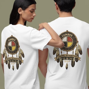 May include: White t-shirts featuring a circular design with the word "LUMBER" and the text "FEDERAL RECOGNITION 12.18.25 575th". The design includes a cross with four colored quadrants and feathers.