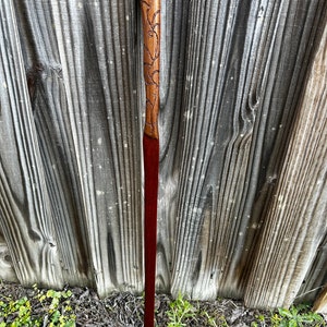 May include: A wooden walking stick with a carved handle featuring a floral design. The handle is a light brown colour and the shaft is a dark red colour.