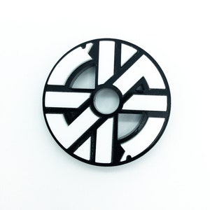 K&ouml;nnte beinhalten: Schwarzer und wei&szlig;er runder Aufkleber mit geometrischem Design. Der Aufkleber hat ein zentrales Loch und ein Muster aus sich kreuzenden Linien.