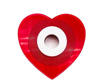Può includere: Un oggetto rosso a forma di cuore con un design a cerchio concentrico bianco al centro.