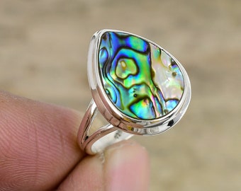 Könnte beinhalten: Ein silberner Ring mit einem tropfenförmigen Einlegeteil aus Abalone-Schale. Die Schale hat schillernde grüne, blaue und violette Farben.